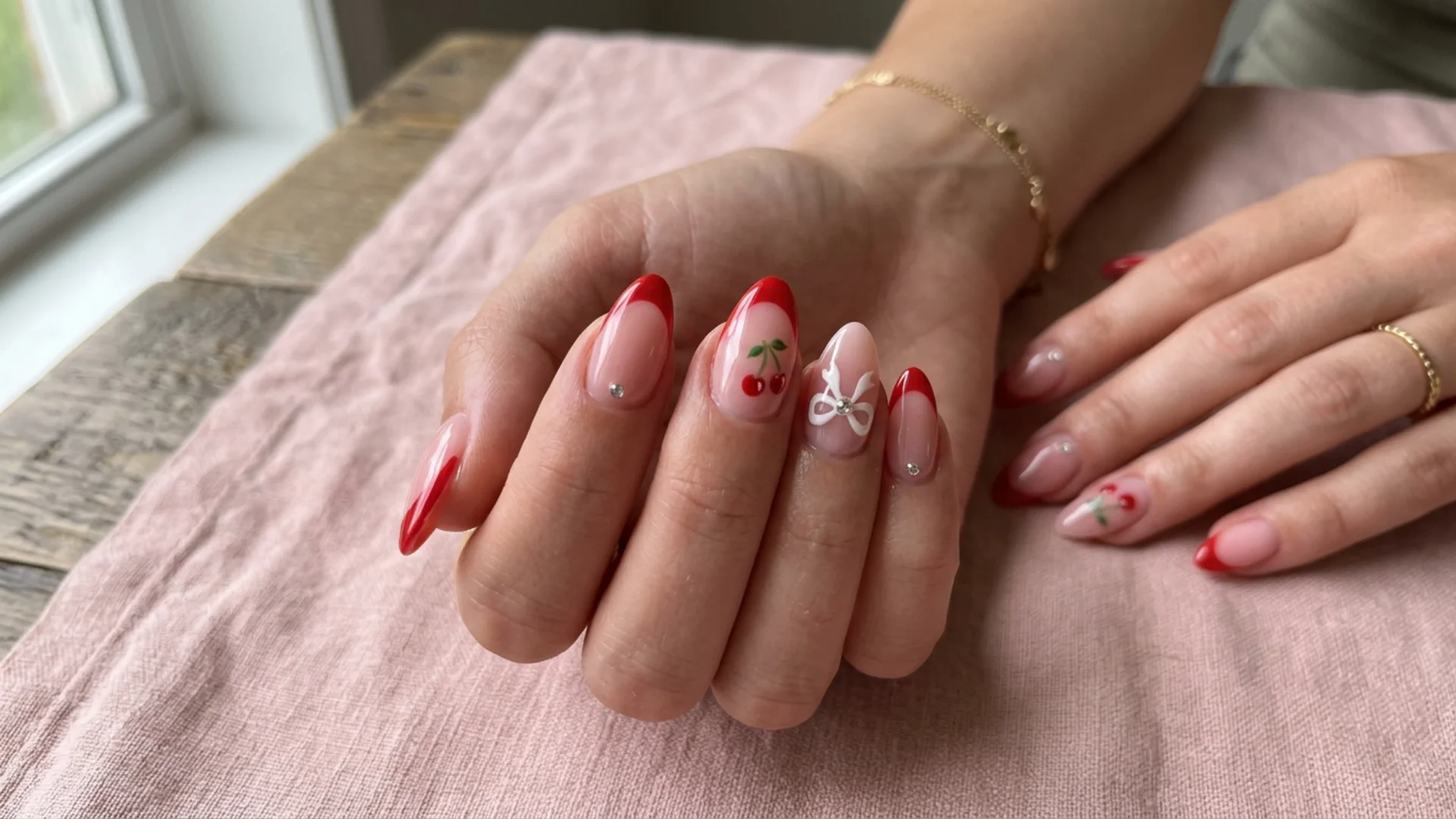 Detailed close up of playful nail design with glossy pink polish, red tips, cherry artwork, and decorative white bows