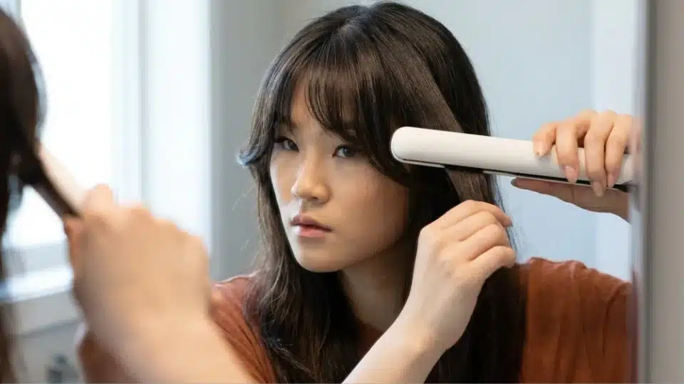 Woman using a flat iron to create a soft outward bend in curtain bangs for a smooth styled finish