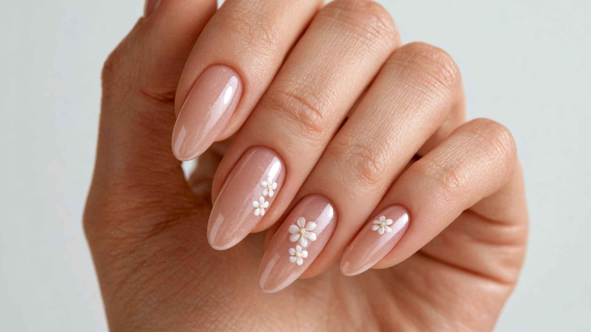 Close-up of glazed donut nails with tiny white floral accents over a sheer pink base and soft pearl chrome shine