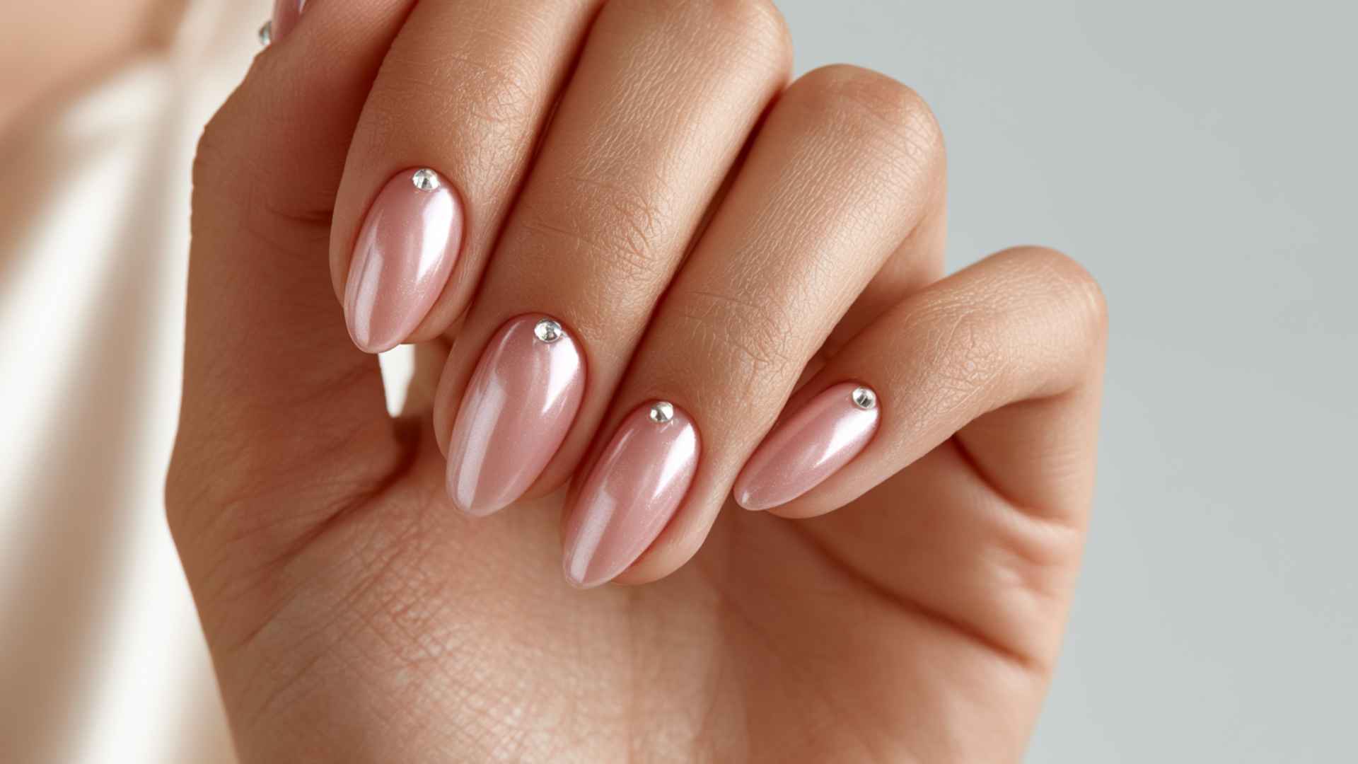 Close up of glazed donut nails with tiny rhinestones near the cuticles and a soft glossy pearl chrome finish in daylight