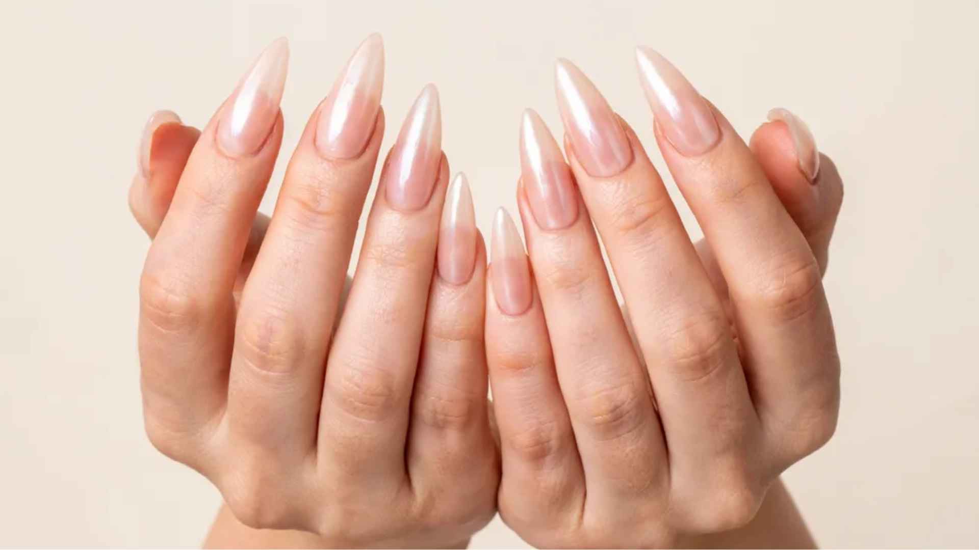 Close-up of pointed stiletto glazed donut nails with a soft nude base and sleek reflective pearl chrome shine in daylight