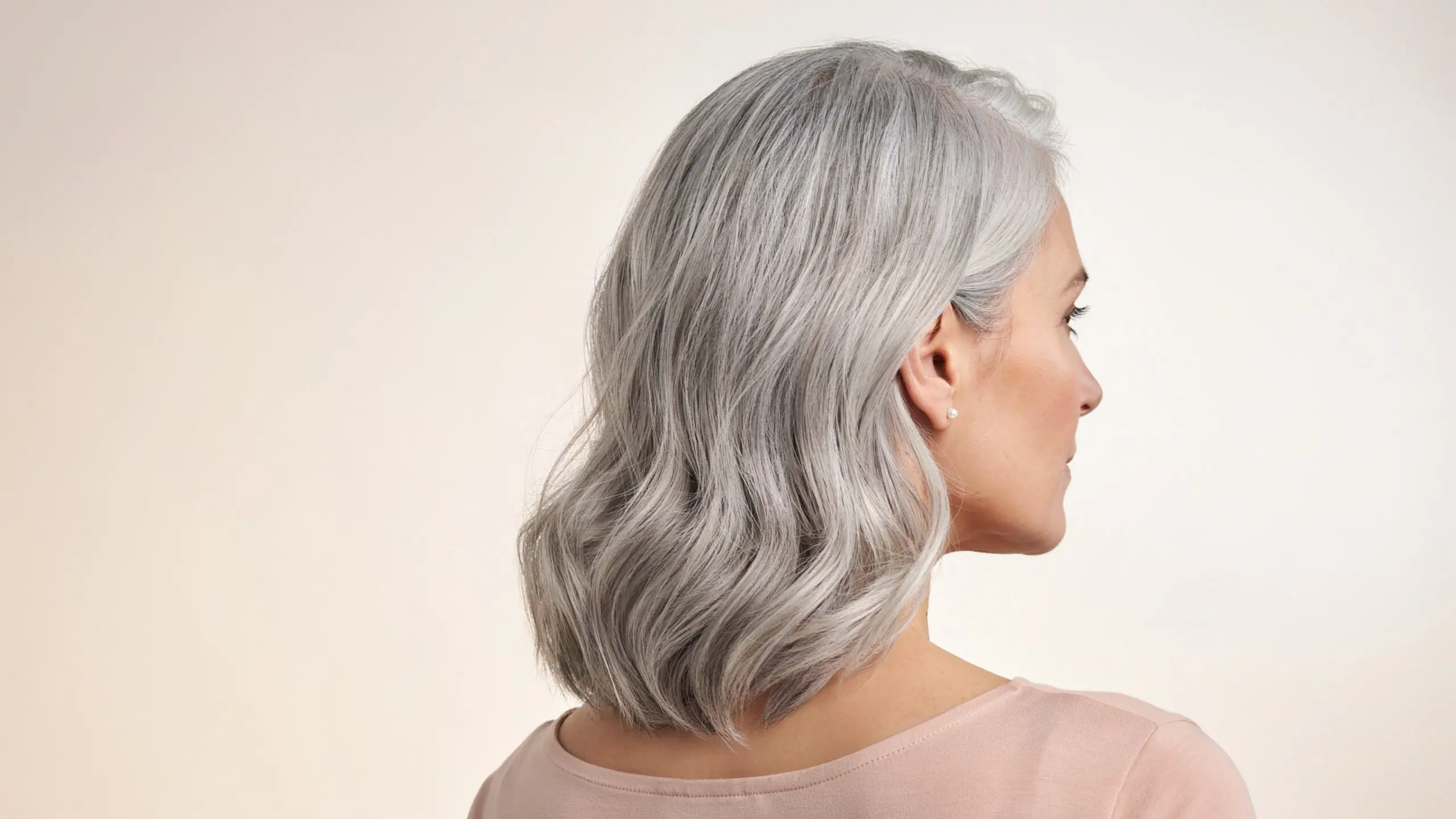 Woman with silver gray wavy hair showcasing a stylish layered haircut from a side profile view.