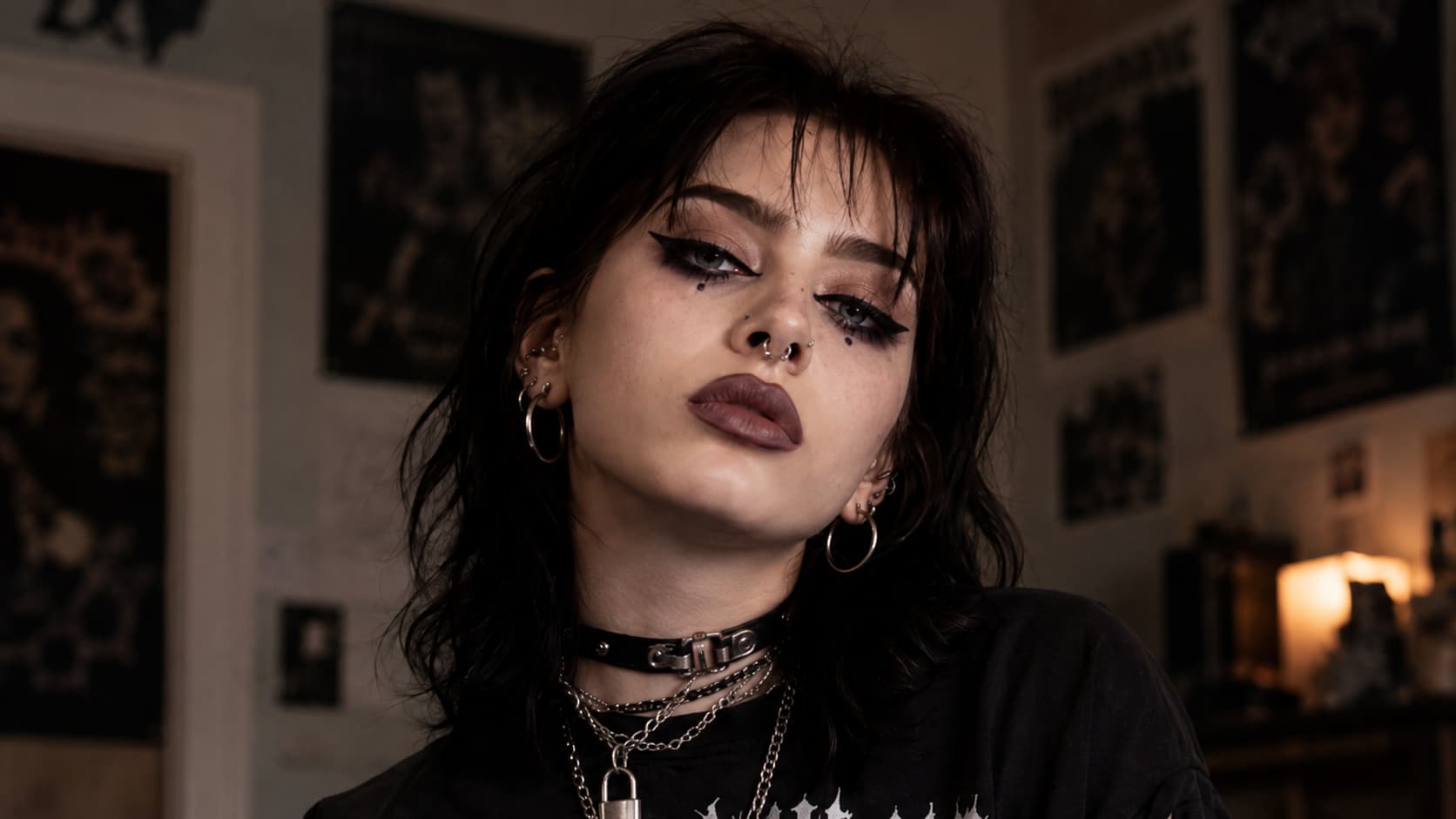 Close-up of a woman with sharp winged eyeliner, dark under-eye accents, berry lips, and a buckled choker.