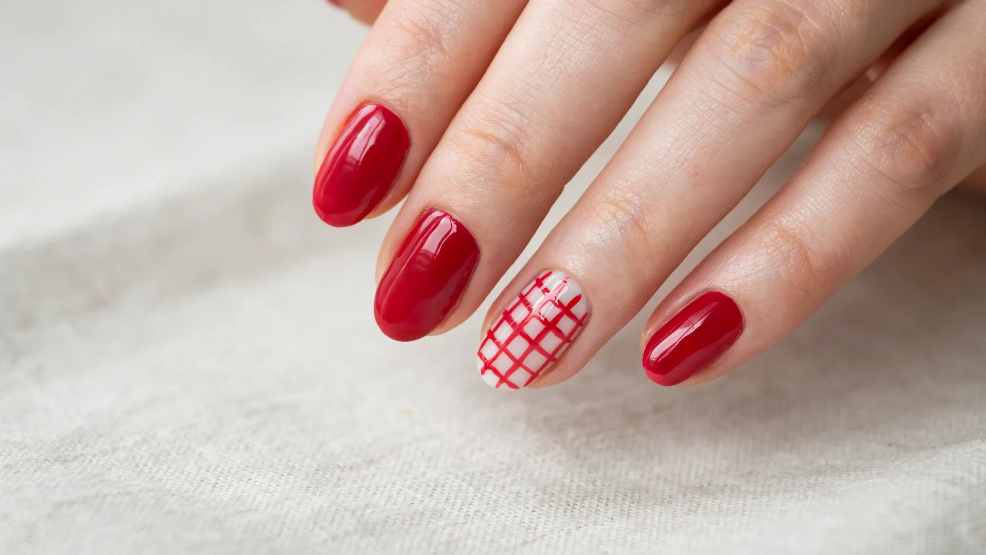 Festive manicure design featuring rich red polish with a white grid patterned accent nail on a neatly shaped hand