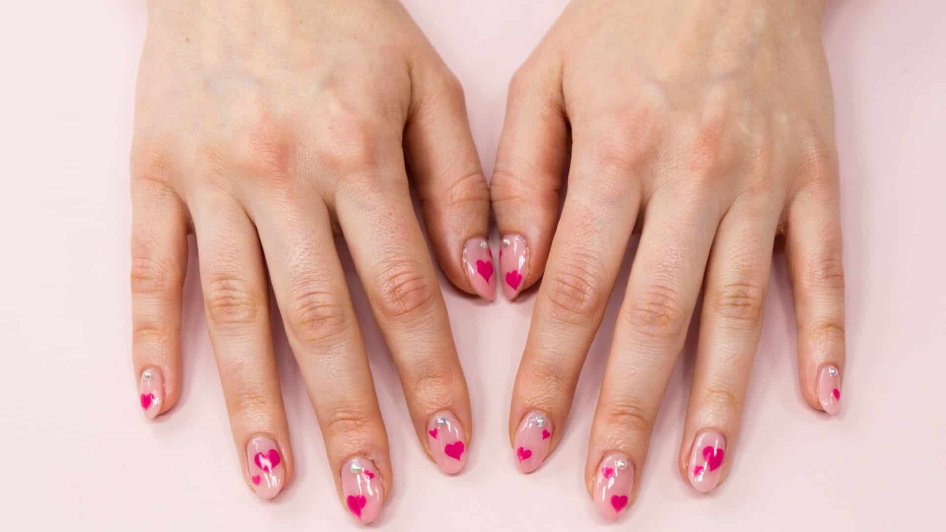 Sheer nude nails with small hand painted hot pink hearts and rhinestone dots.