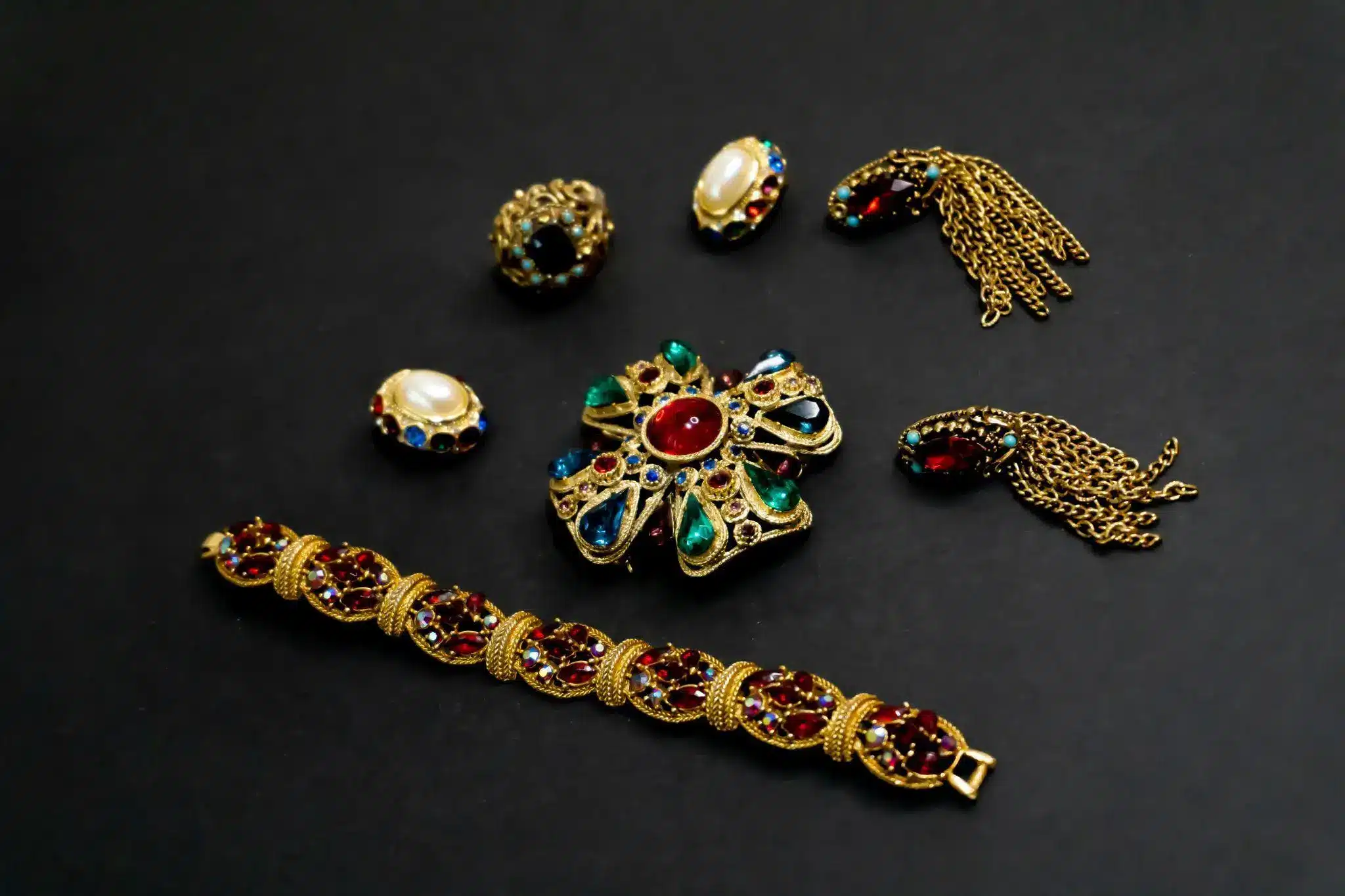 Vintage jewelry collection with ornate gold brooch, bracelet, and earrings against black background