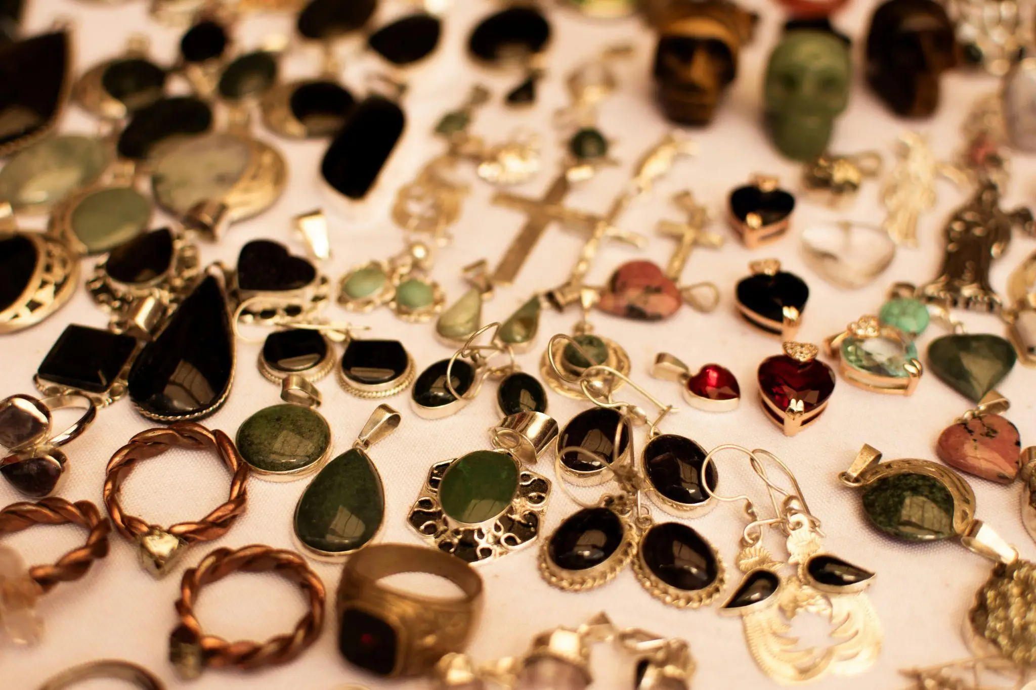 Various gemstone pendants and rings displayed on a white cloth in warm lighting