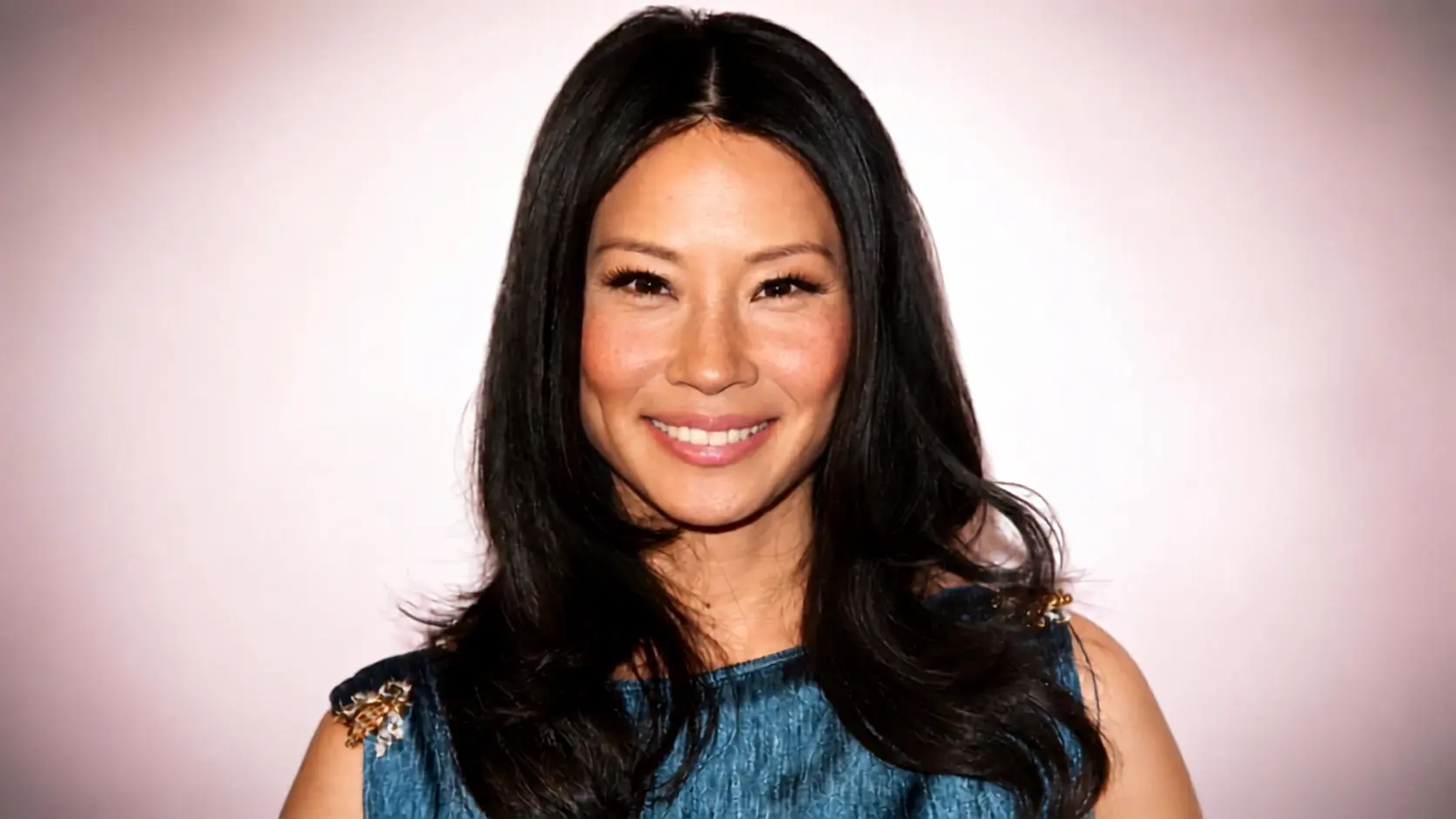 Lucy Liu with long black layered hair and a center part, wearing a blue dress at a formal event with soft waves.