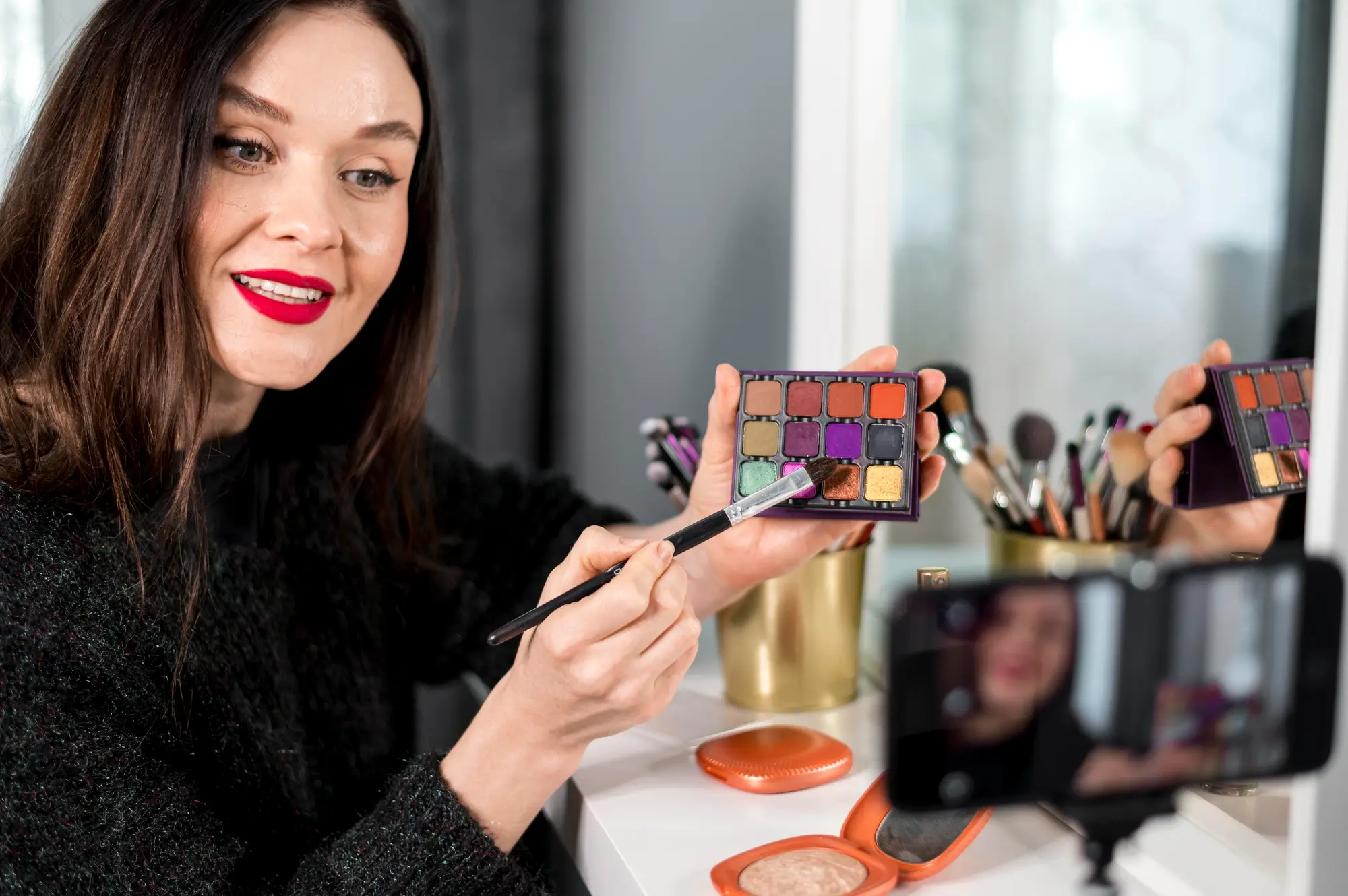 Makeup artist demonstrating eyeshadow palette using a brush in a beauty tutorial setup