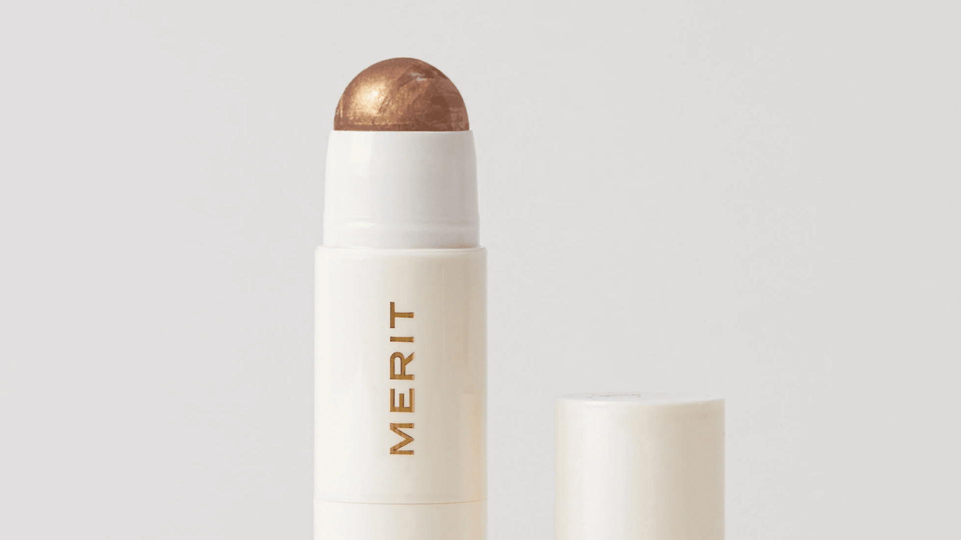 Merit Day Glow Highlighting Balm stick with cream highlighter texture shown against a clean white background