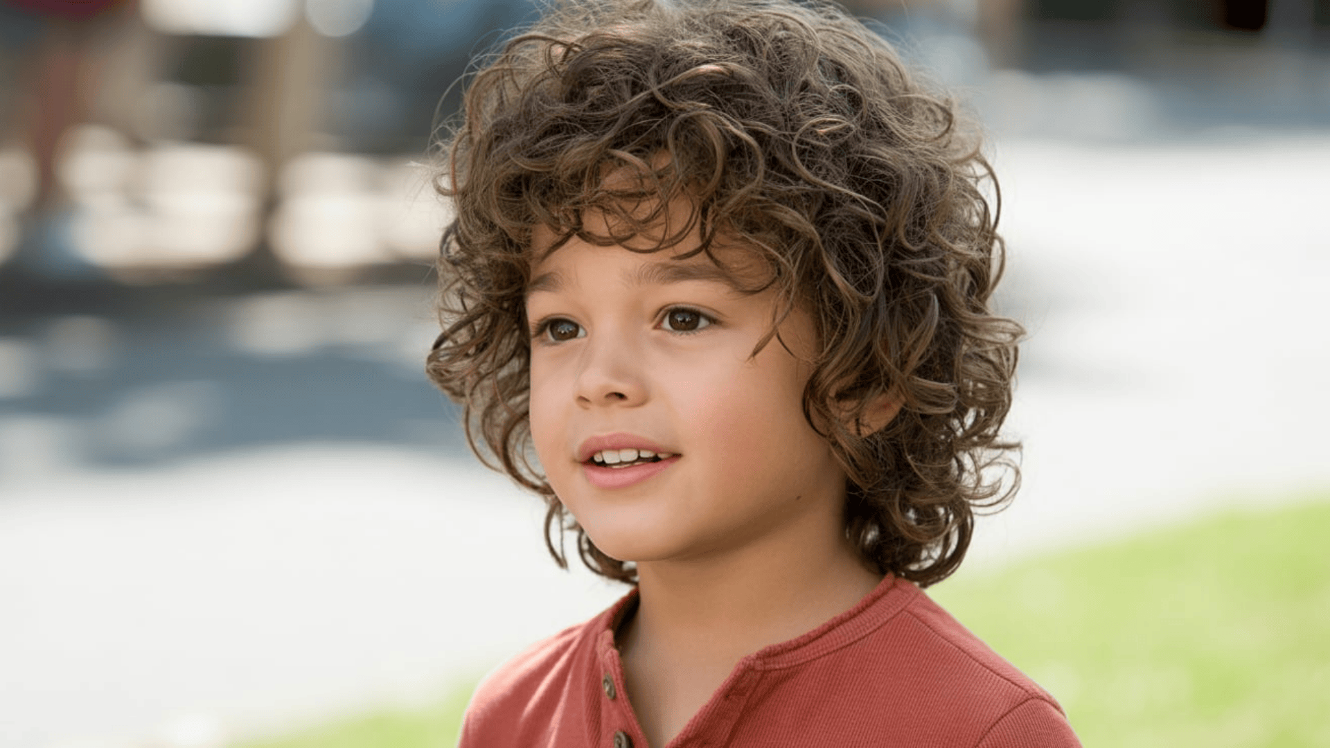 Boy with messy curly hairstyle featuring natural volume and tight curls, smiling outdoors in soft daylight.