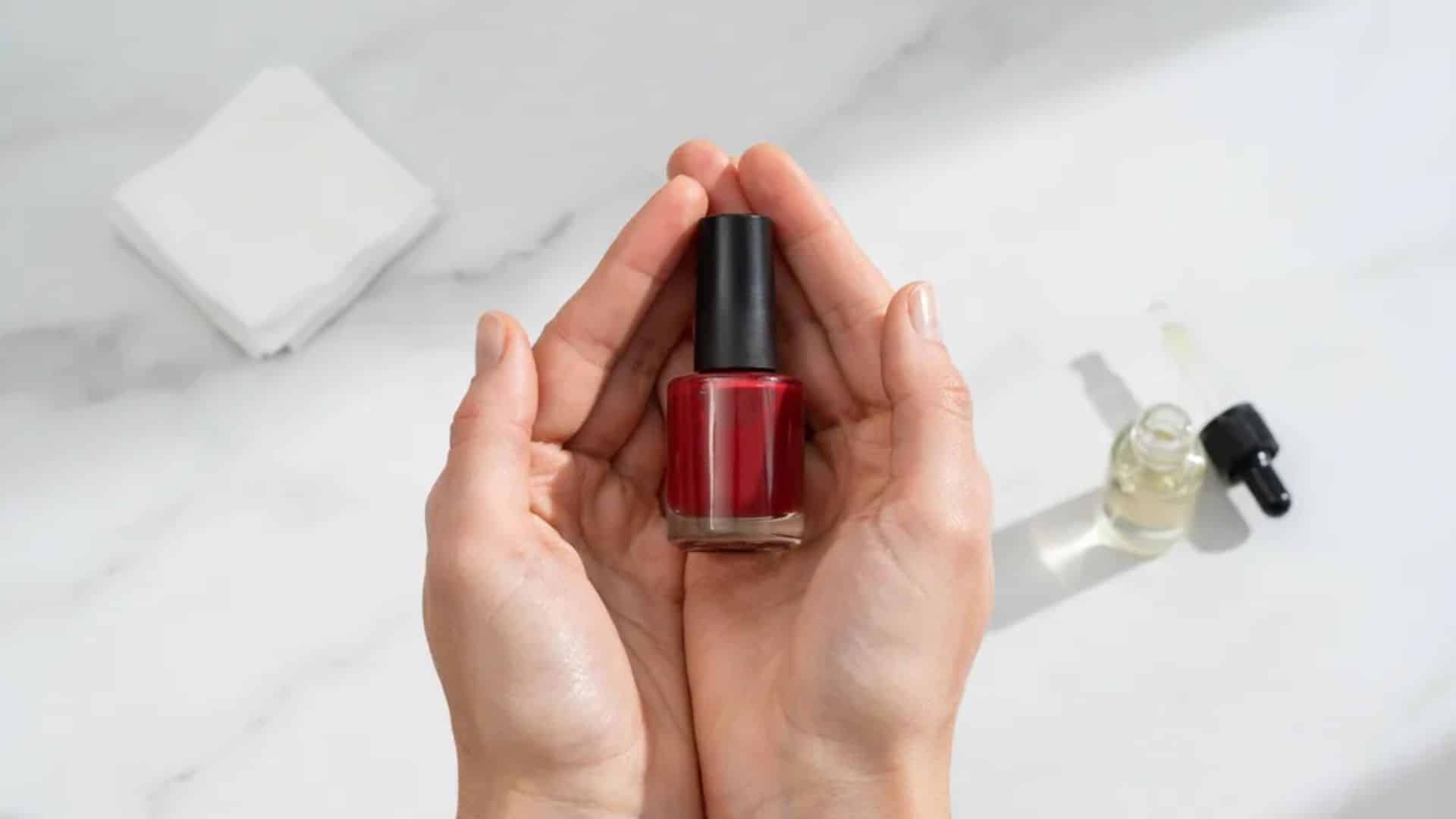 Rolling a deep cherry red nail polish bottle between hands to blend thinner evenly
