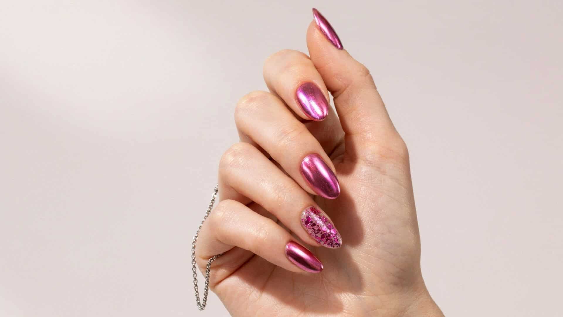 Hand with almond shaped neon pink chrome nails and one glitter accent nail, close up view