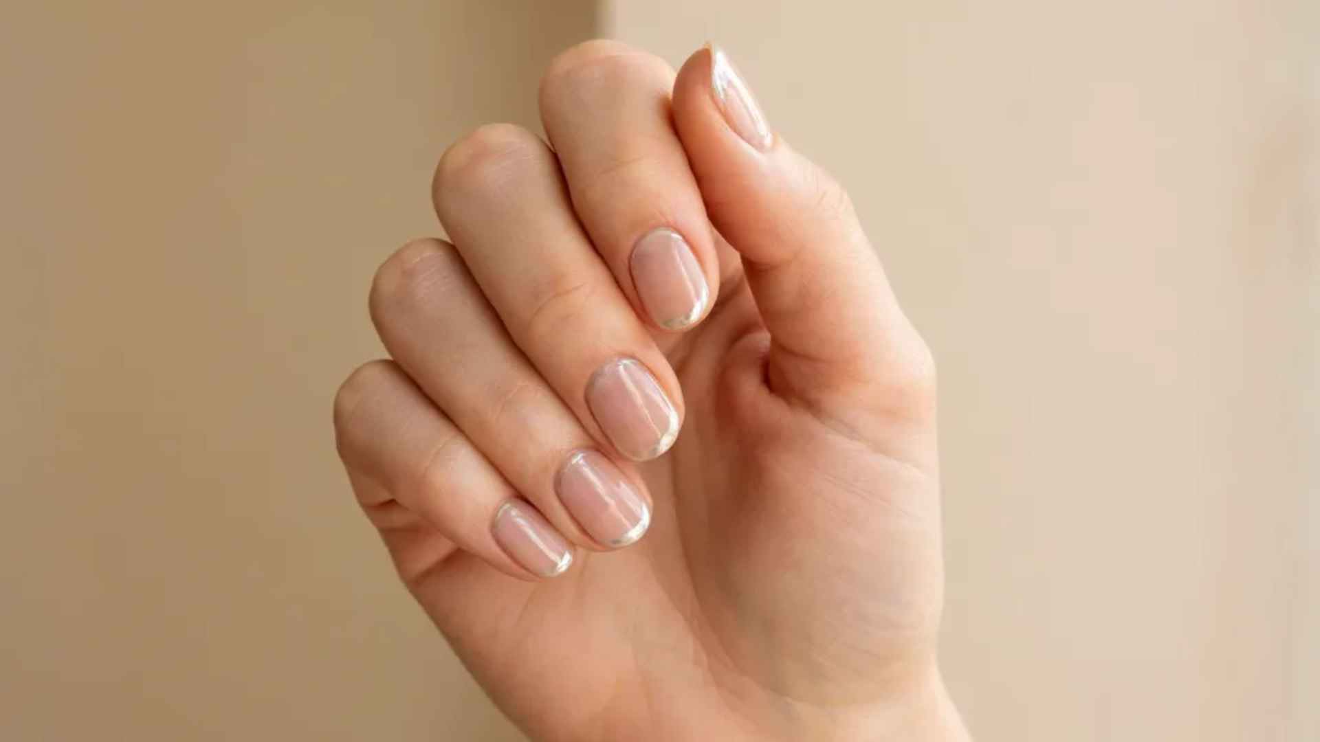 Close up of nude glazed donut nails with a sheer beige base and a natural glossy pearl chrome finish in soft daylight