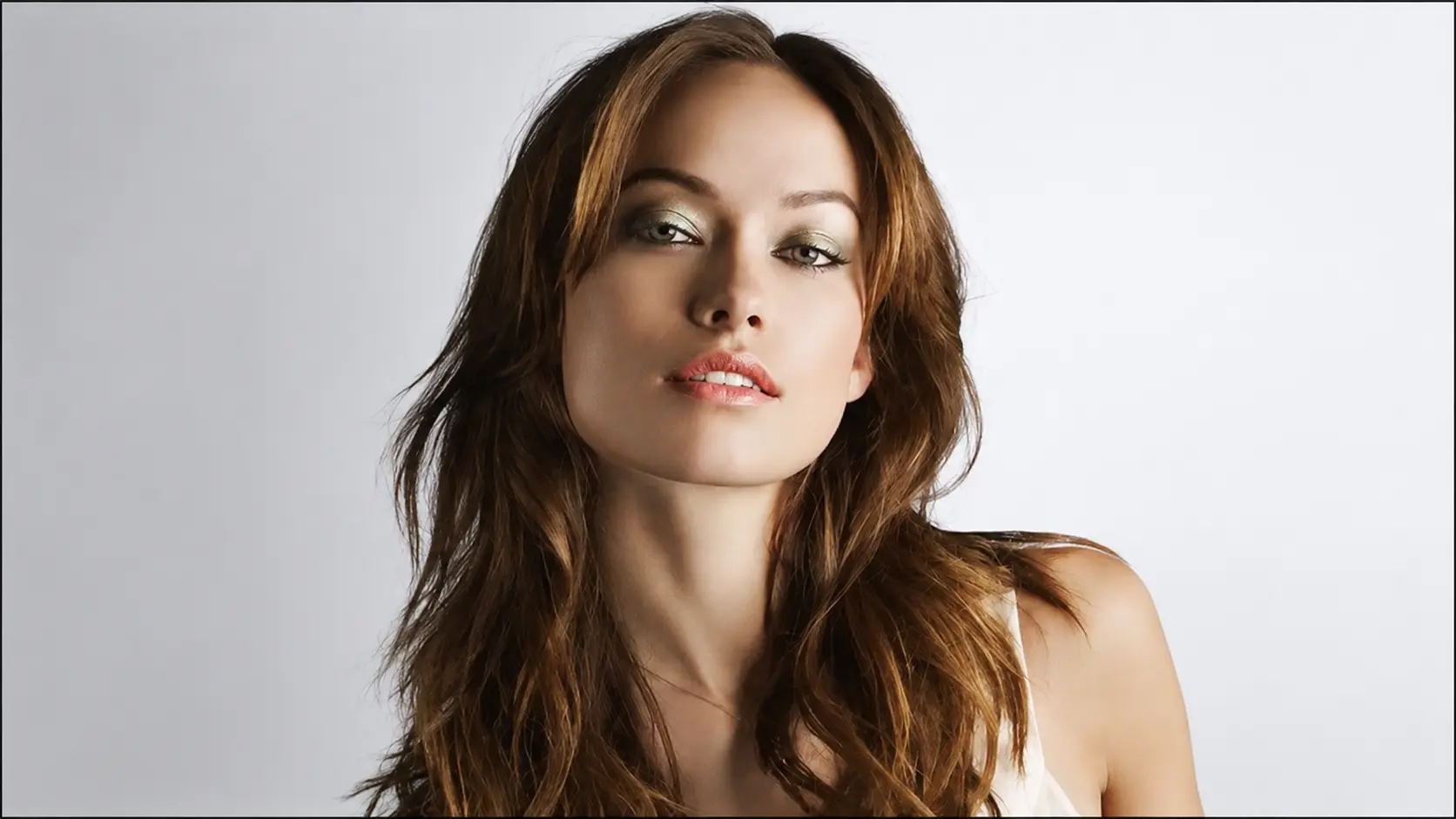 Portrait of Olivia Wilde with long brown hair and soft makeup posing against a light background in a studio setting.