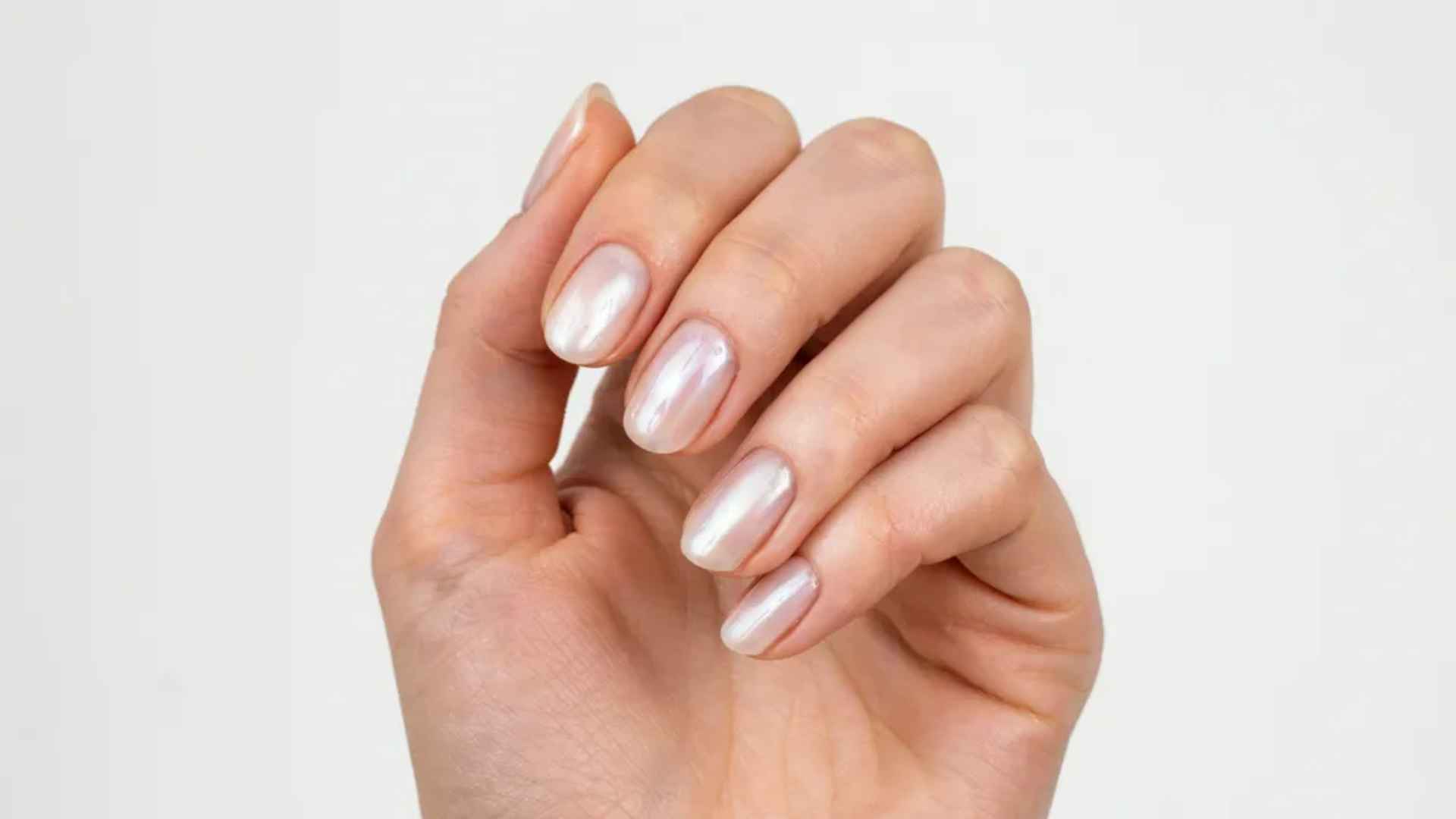 Close up of pearl white glazed donut nails with a bright milky base and luminous reflective chrome shine in daylight