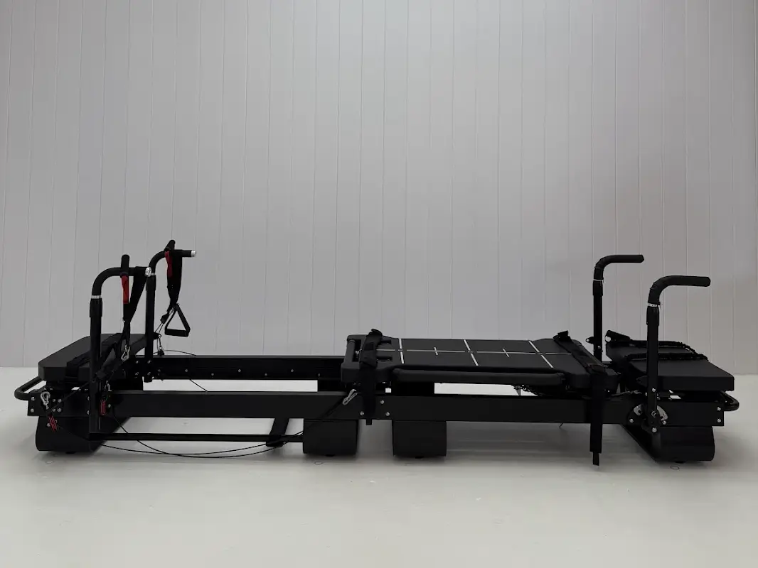 Black Pilates reformer machine in minimalist studio with white paneled walls