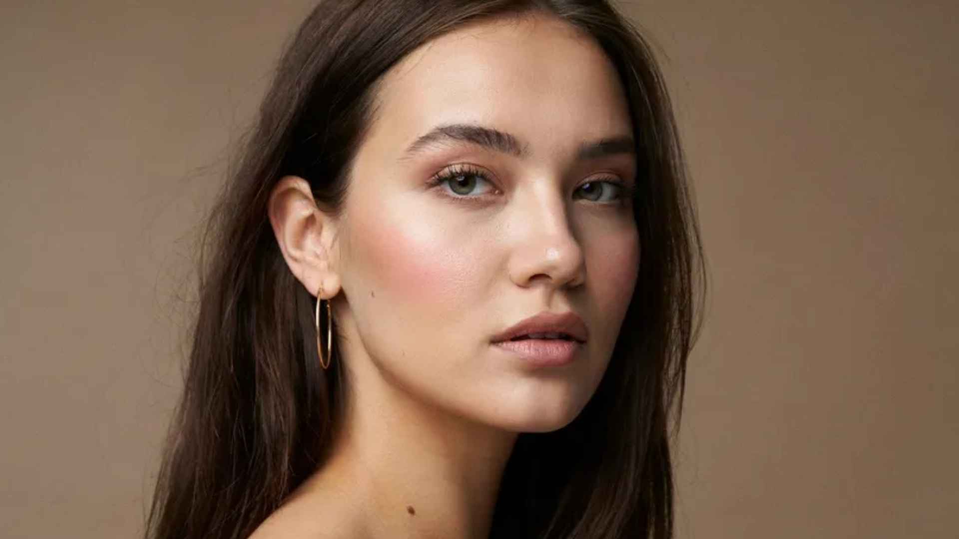 Woman wearing soft natural glam makeup with defined lashes, deeper blush, neutral lips, and fresh skin finish