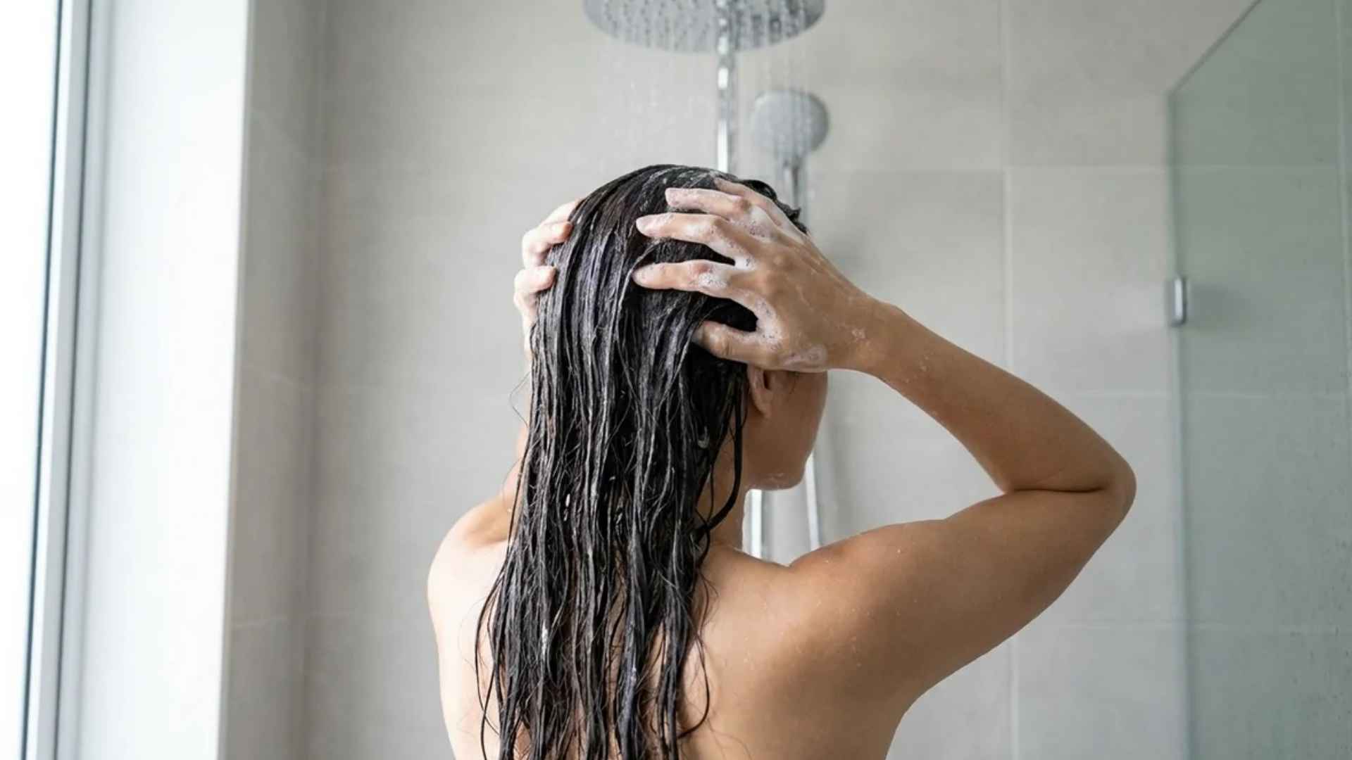 Woman gently squeezing water from wet hair with soft towel after hair wash routine