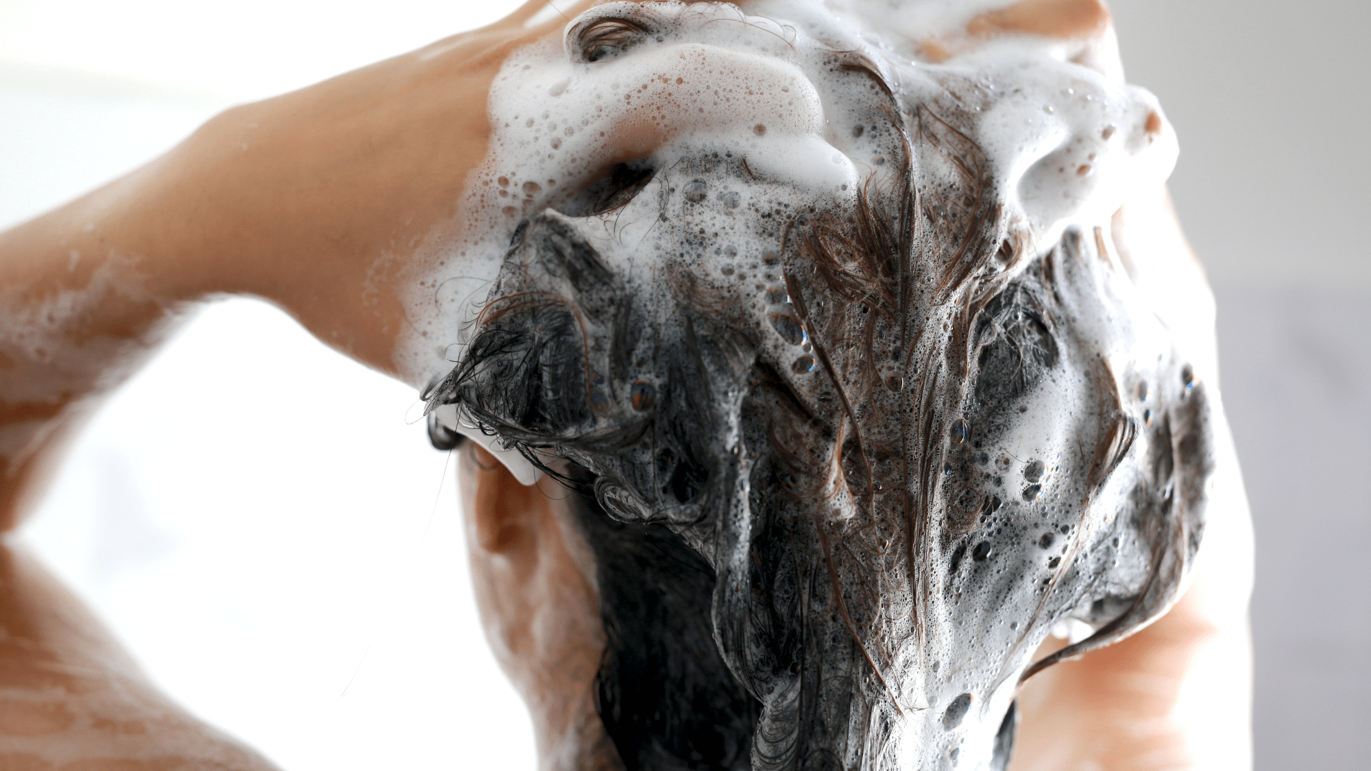 Close-up of hair being washed with shampoo foam during wash routine to protect and maintain healthy honey and caramel highlights.