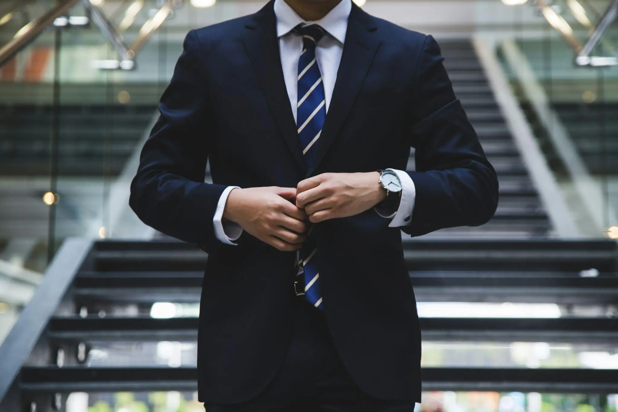 Man in dark suit buttoning jacket in modern office stairway with glass railings