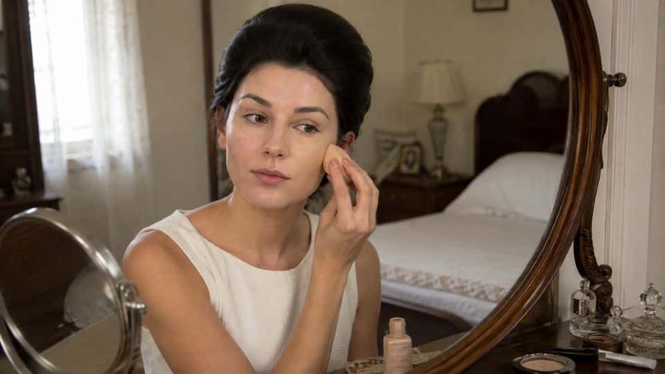Woman applying foundation with a makeup sponge to create a smooth matte base for a 1960s makeup look