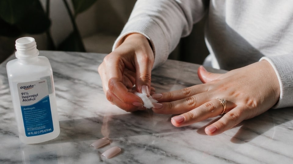 Rubbing alcohol applied near a press on nail edge to help loosen adhesive during removal
