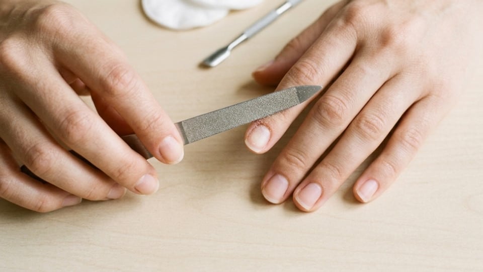 Hands holding a nail file at the corner of a short nail while shaping the edge gently for a rounded finish now