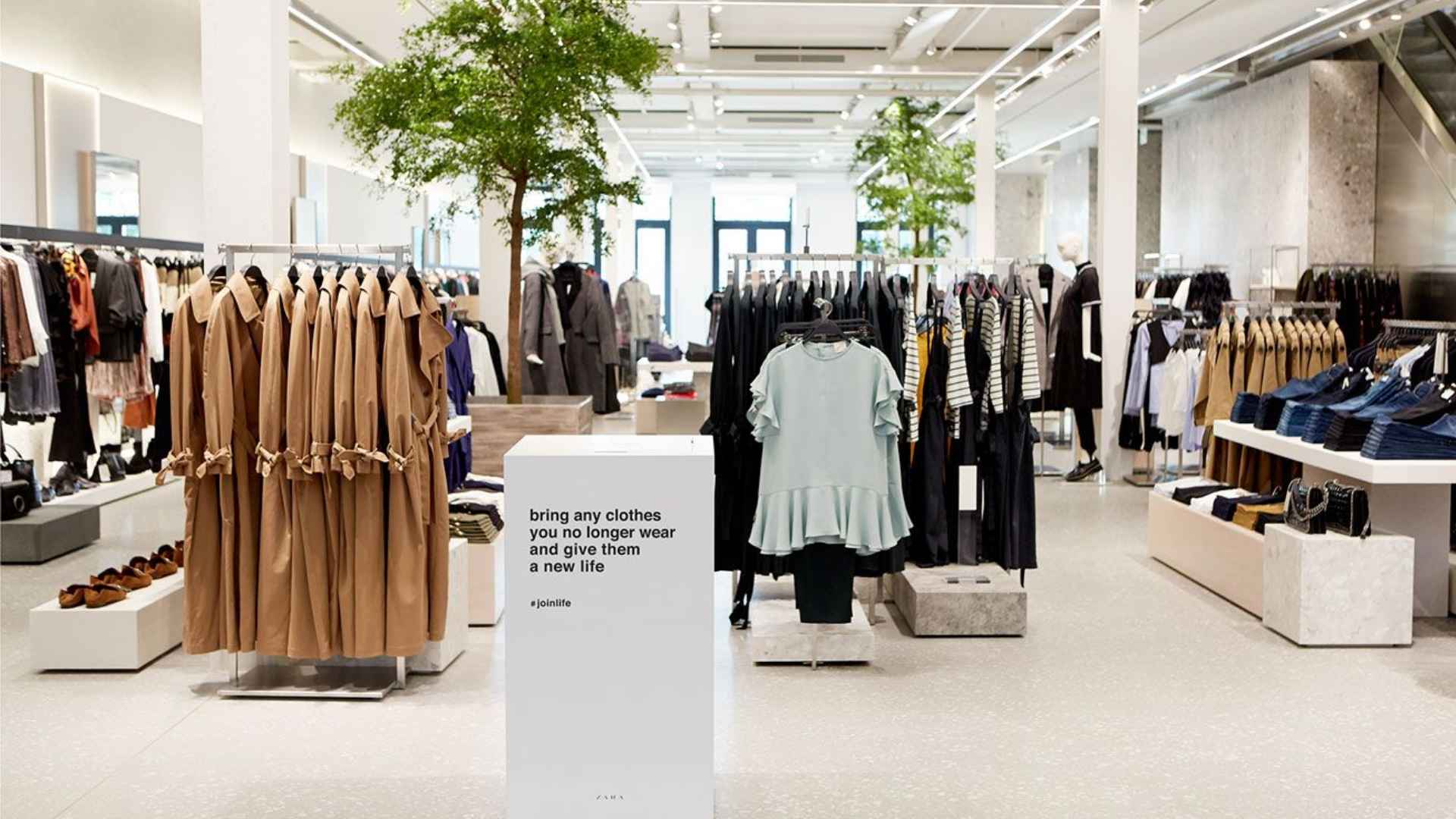Bright Zara store interior with neatly arranged clothing racks and a clothing donation collection point promoting garment recycling.