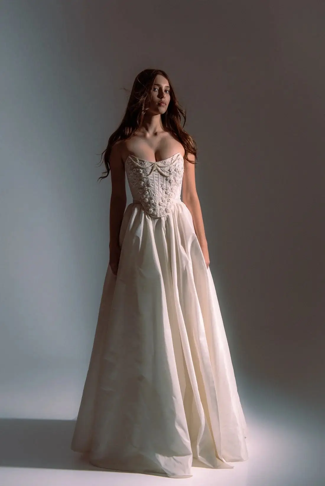 Brunette woman in elegant white strapless gown posing under soft studio lighting