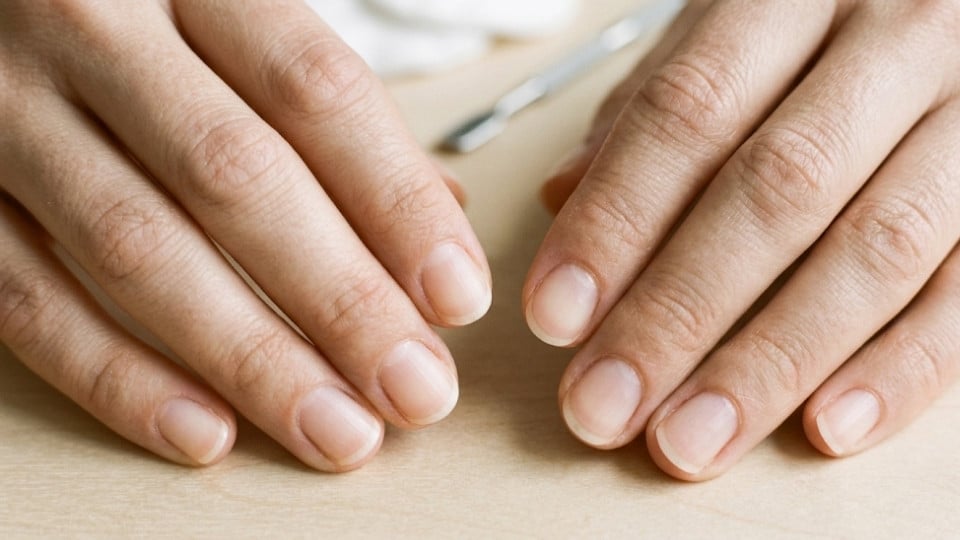 Hands displaying finished short rounded nails with smooth edges on a beige manicure table showing a clean manicure result