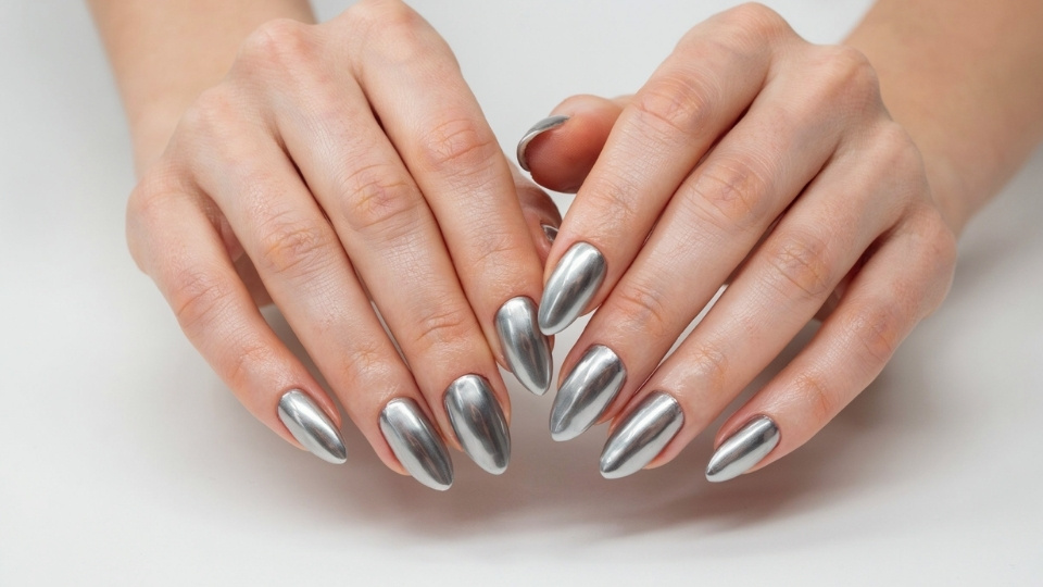 Long almond shaped nails covered in silver chrome polish with a smooth reflective finish