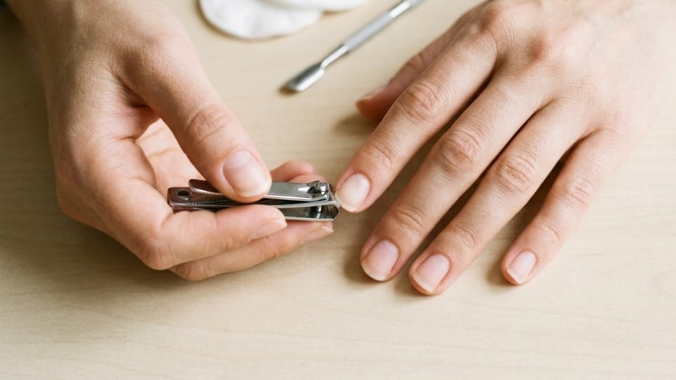Hands using a nail clipper to trim short natural nails straight across on a clean surface for a round nail shape