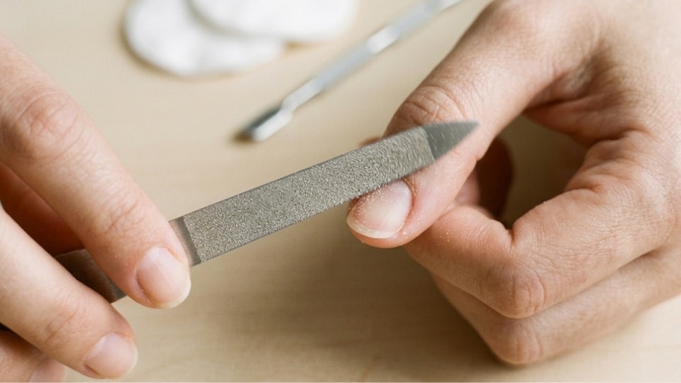 Hands filing the side of a natural nail toward the center to create an even curved round shape with careful technique