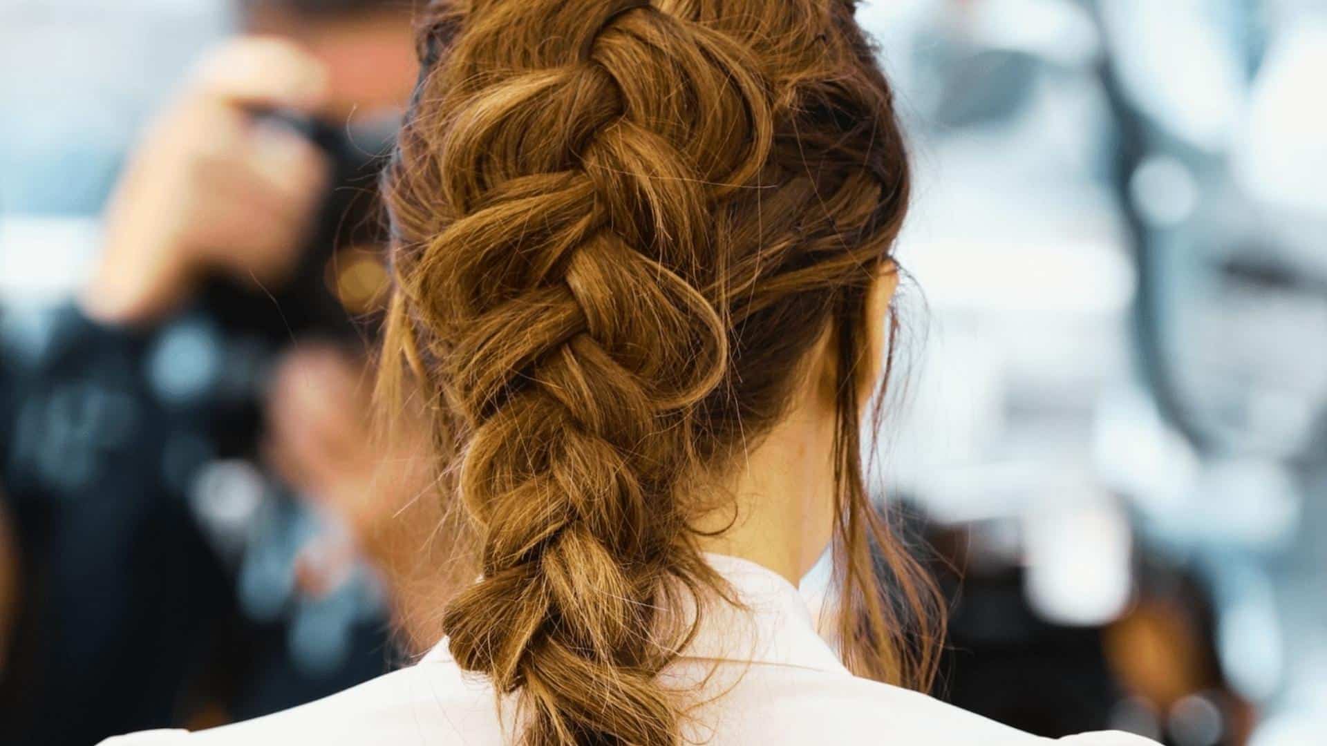 Close view of an auburn Dutch style braid from the back, showing its raised woven texture against a softly blurred background