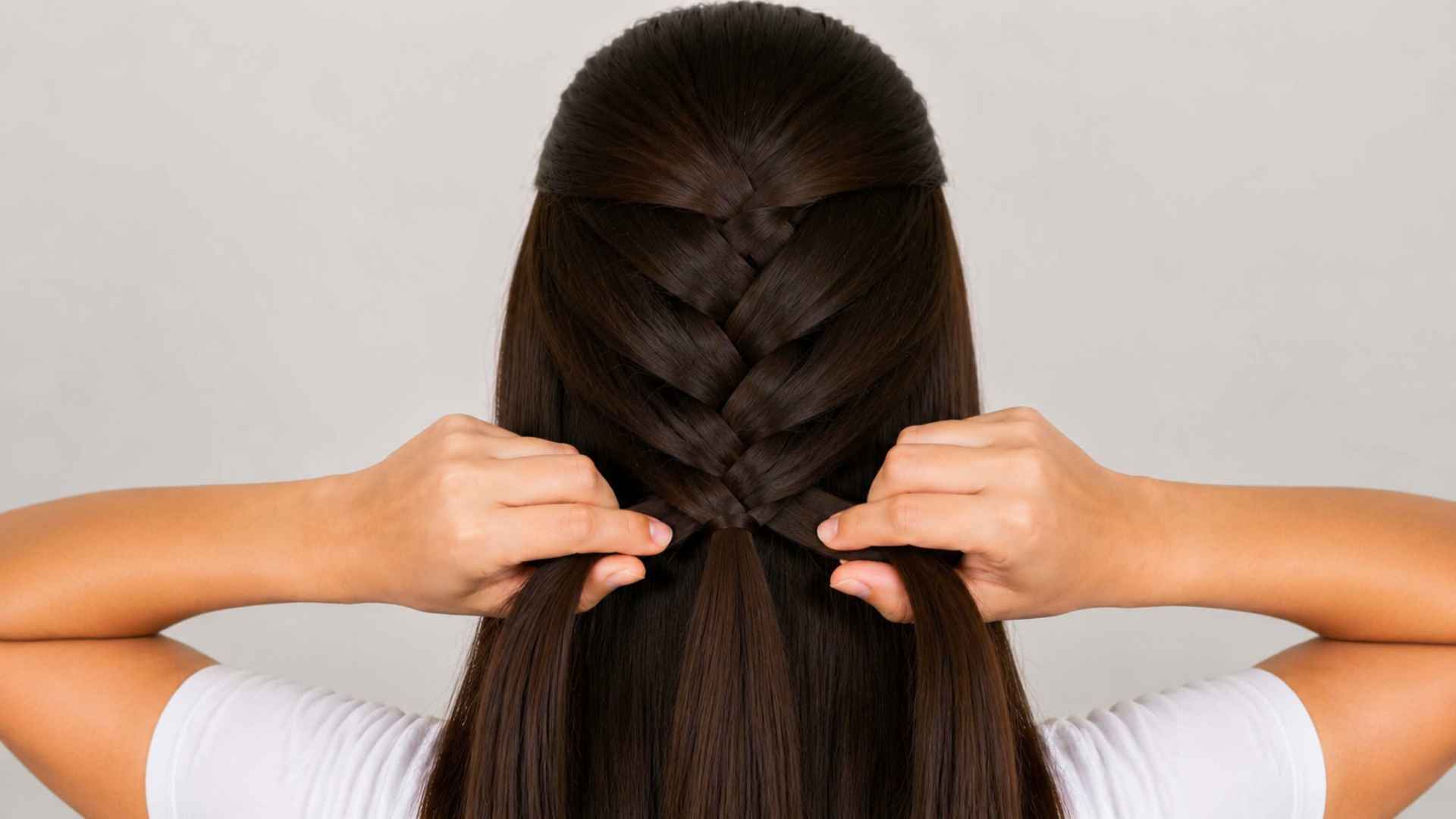 French braid continuing down the back of the head with hands holding the side sections in place