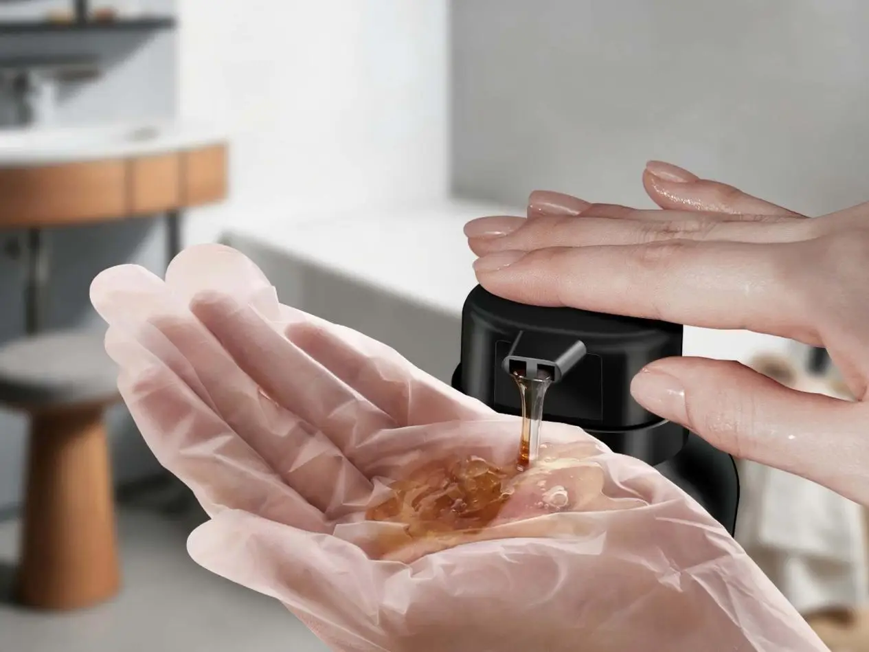 Hands wearing gloves pumping liquid soap from a black dispenser in a bathroom setting