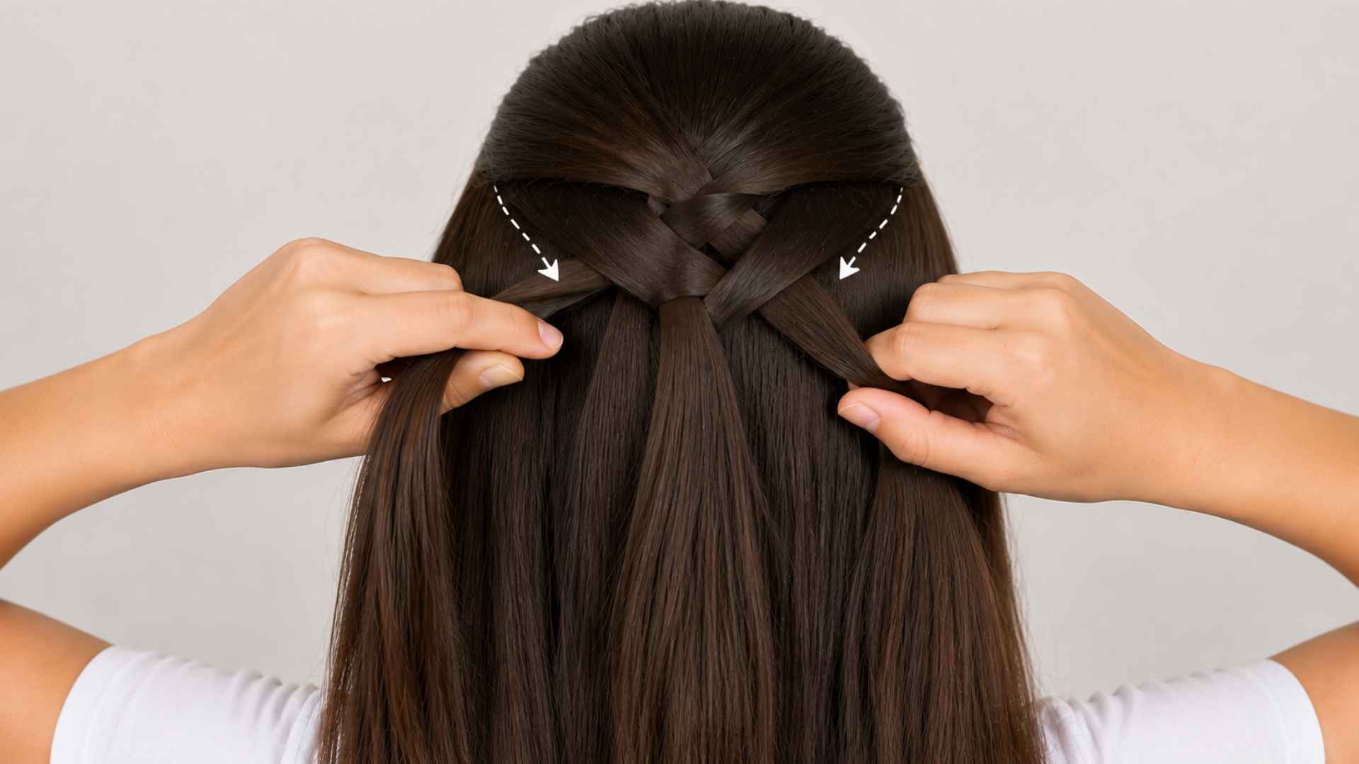 Hands adding new hair sections while crossing strands to build a French braid down the back of the head