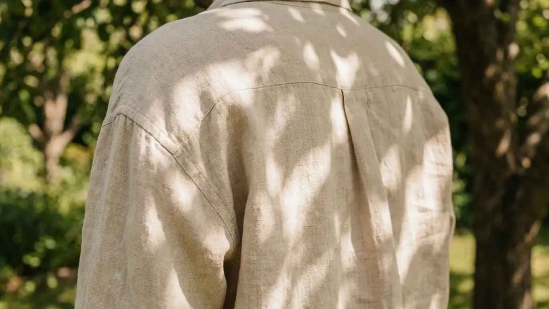 Person in loose linen shirt standing outdoors in dappled tree shade