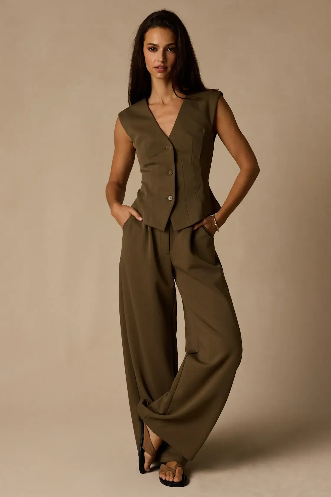 Woman in olive green vest with matching wide-leg pants against neutral background