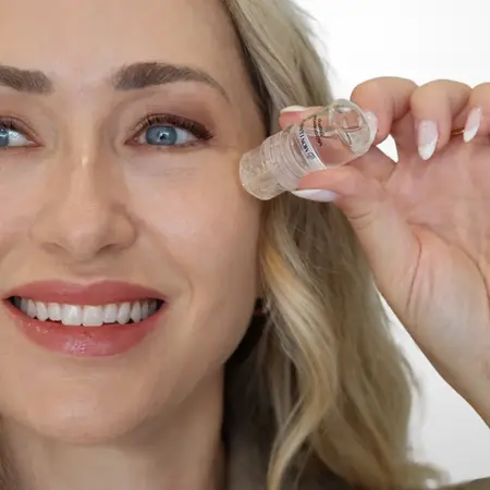 Woman applying serum to face with small clear bottle in bright setting