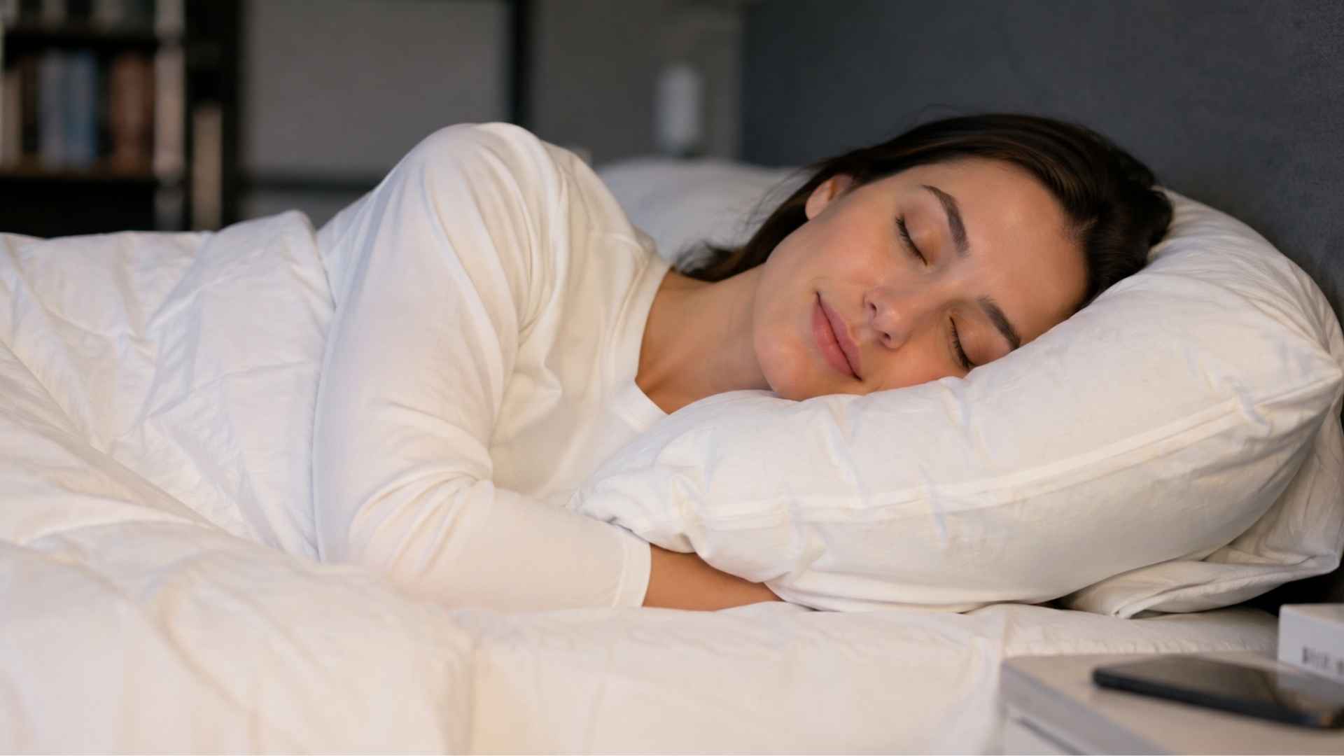 Woman sleeps peacefully on her side in white bedding with her head resting on a soft pillow at night