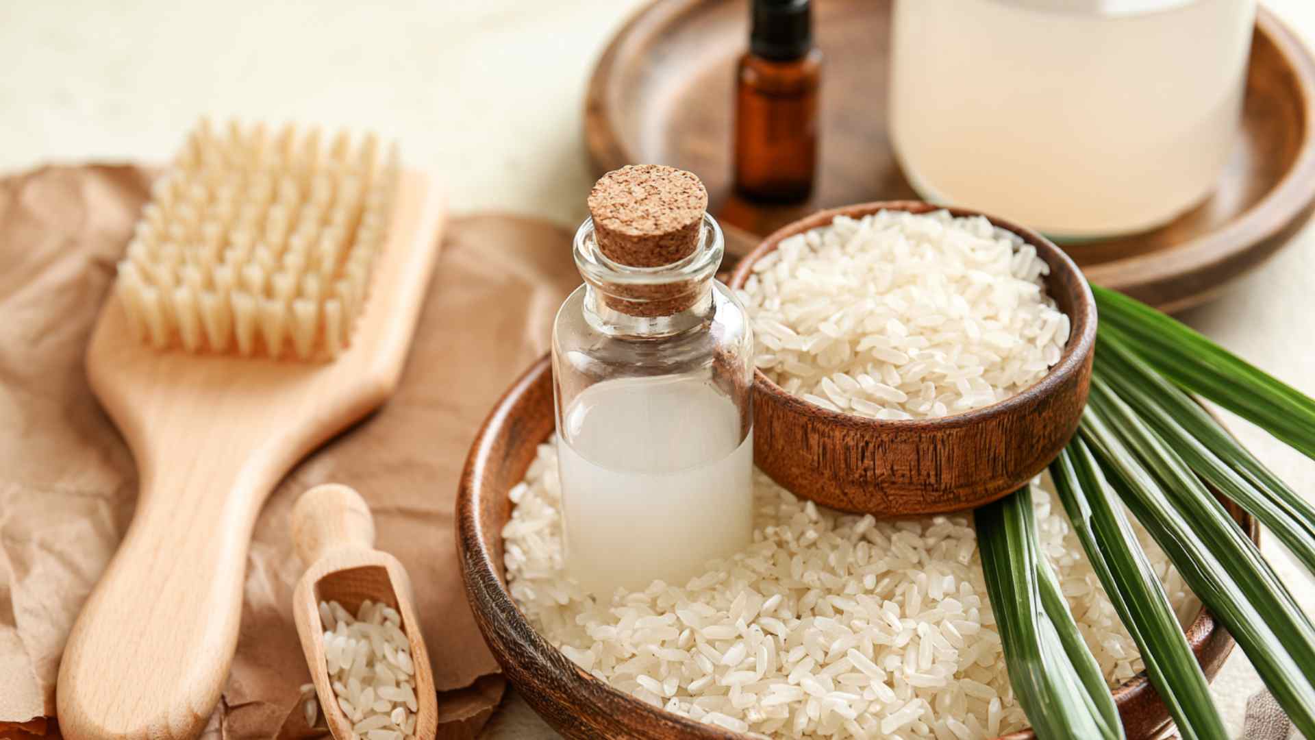 Homemade rice water in a glass bottle surrounded by uncooked white rice and hair care tools