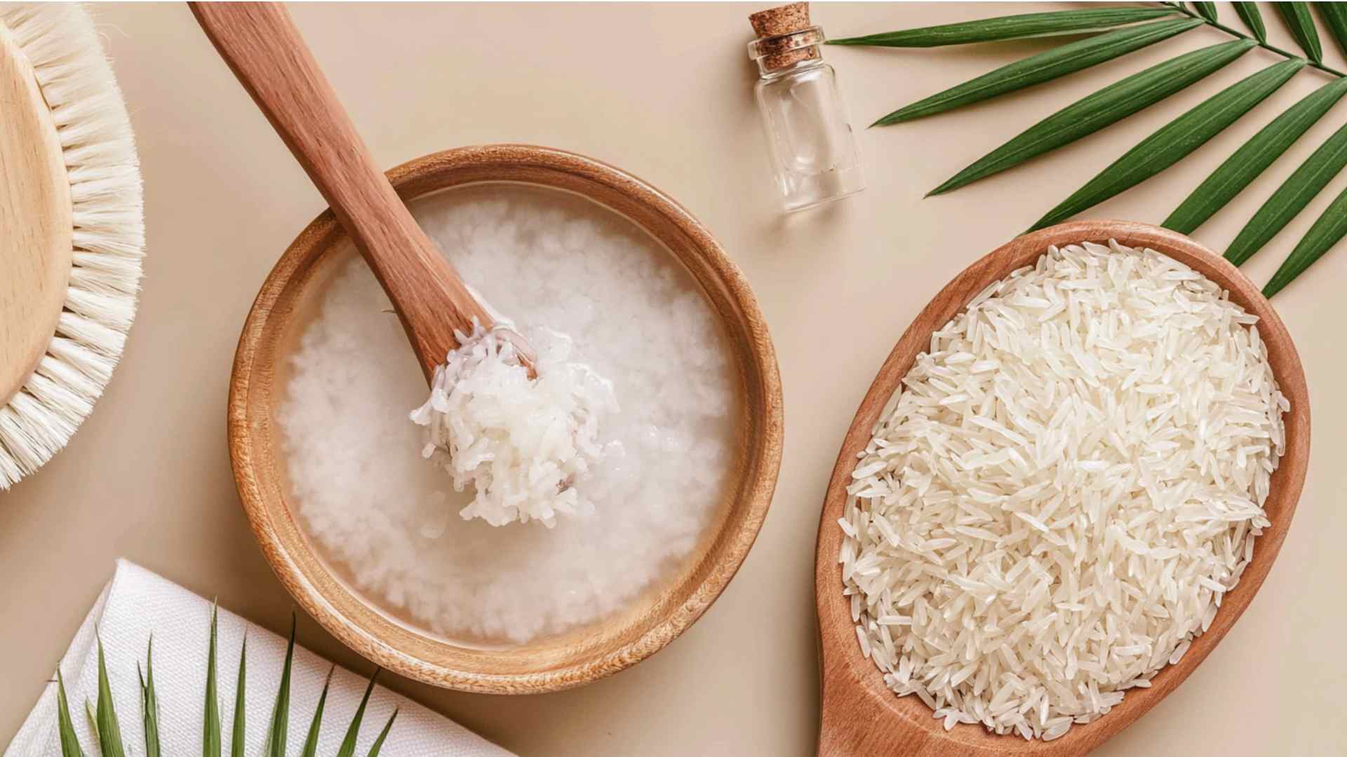 Homemade rice water in a wooden bowl surrounded by uncooked white rice and hair care tools
