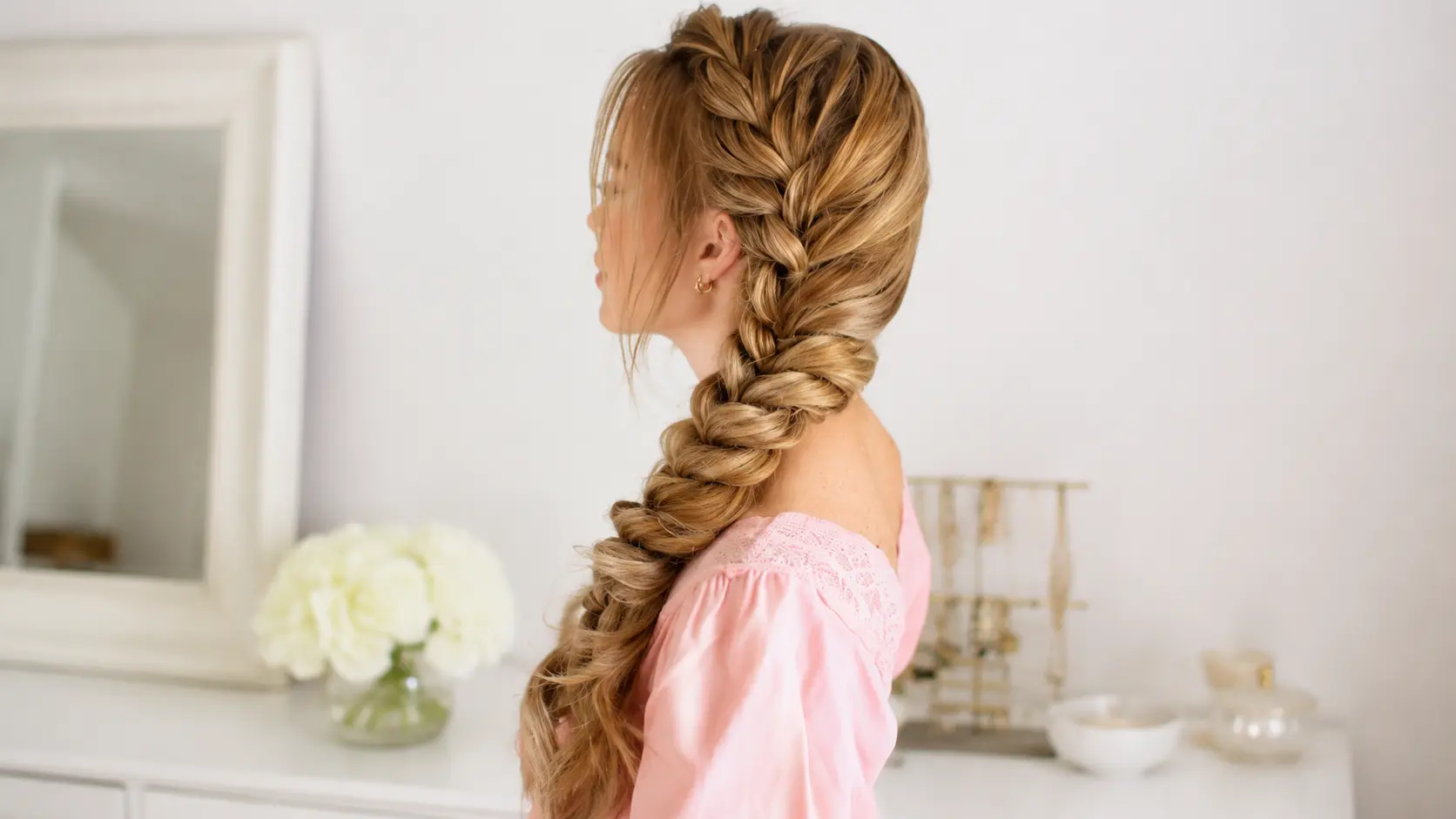 Side profile of a woman with long blonde hair styled in a voluminous Dutch braid draped over her shoulder.