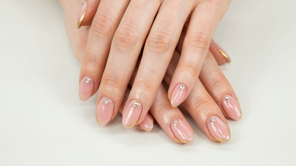 Close up hands showing long almond nails with small crystals and luxury manicure finishes
