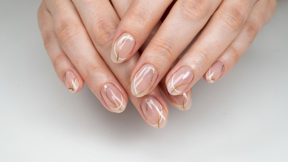 Close up hands showing oval shaped nails with fine curved lines over a soft nude polish base