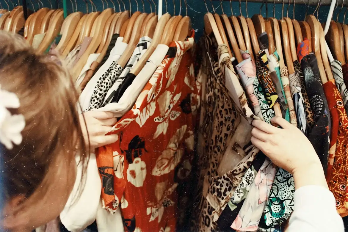 Person browsing colorful patterned shirts on wooden hangers in a wardrobe closet