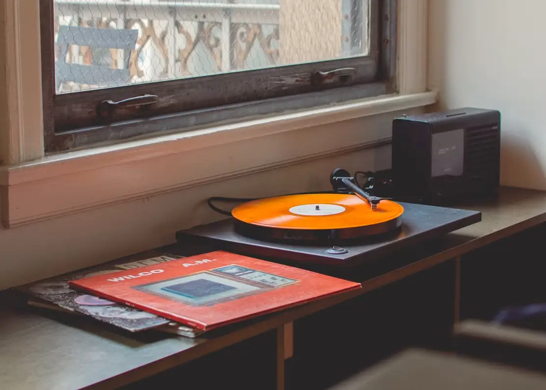 Orange vinyl record playing on turntable near window in cozy indoor setting