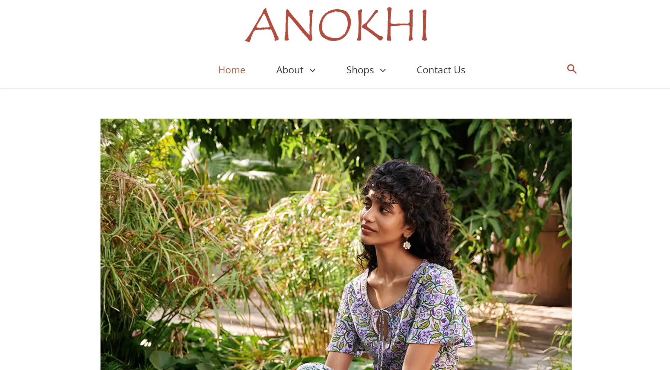 Woman in a purple floral print dress sitting outdoors among lush green foliage.